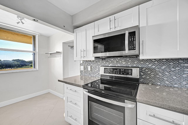 kitchen with dark stone counters, light tile patterned floors, appliances with stainless steel finishes, tasteful backsplash, and white cabinetry