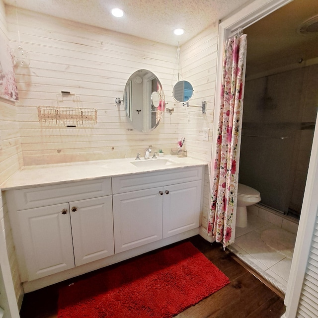 bathroom featuring wood walls, hardwood / wood-style floors, a textured ceiling, toilet, and vanity