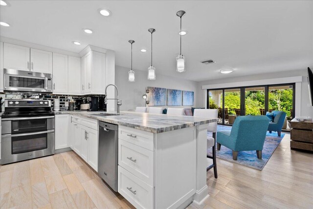 kitchen featuring light stone countertops, appliances with stainless steel finishes, sink, decorative light fixtures, and white cabinets