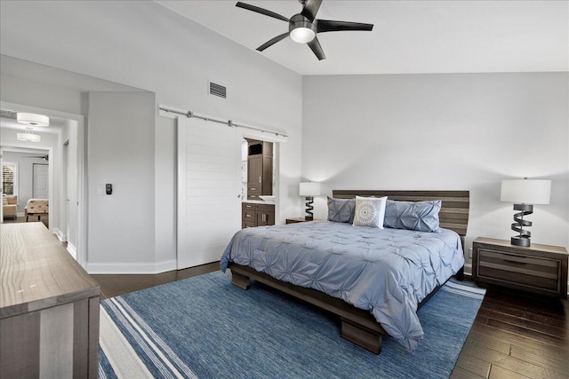 bedroom featuring lofted ceiling, ceiling fan, dark hardwood / wood-style floors, a barn door, and connected bathroom