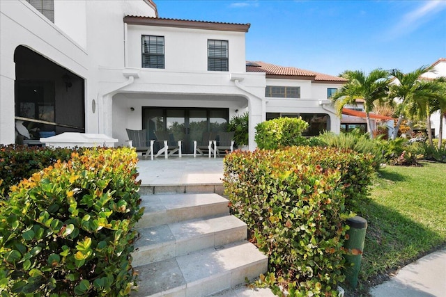 view of exterior entry featuring a lawn and a patio