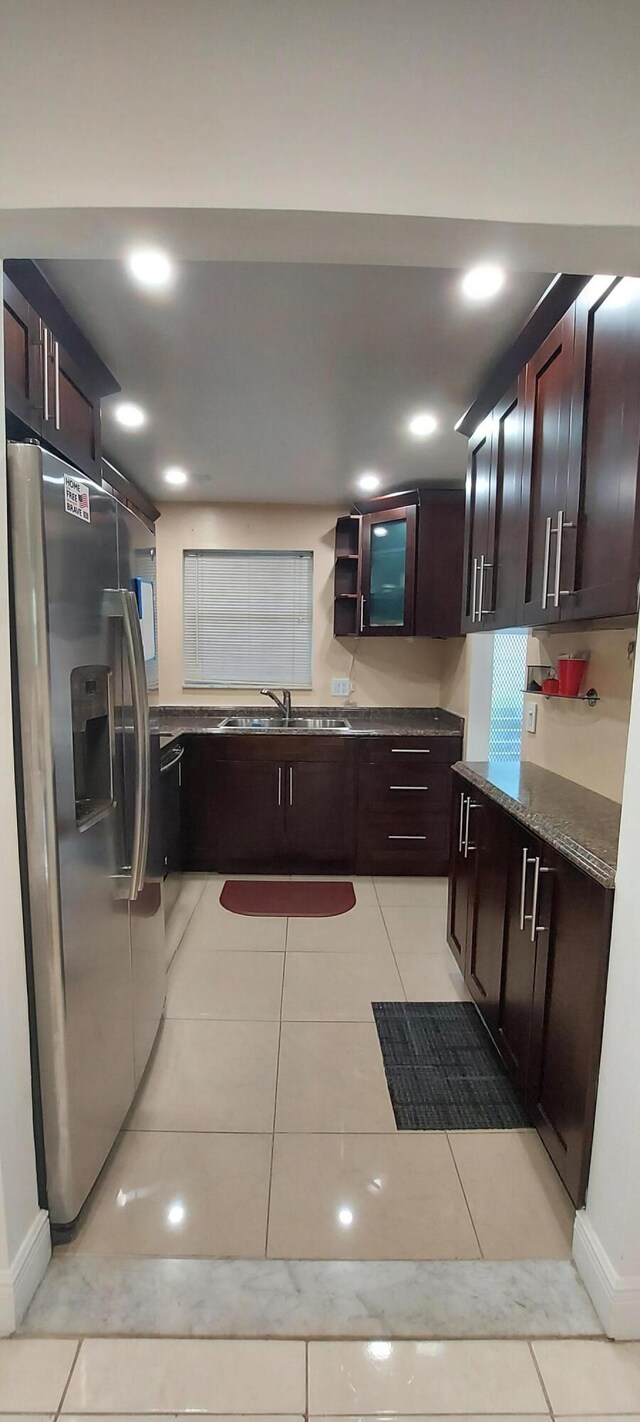 kitchen with stainless steel refrigerator with ice dispenser, light tile patterned floors, dark stone counters, and sink