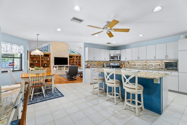 kitchen with pendant lighting, a kitchen island with sink, white cabinets, light stone counters, and stainless steel appliances