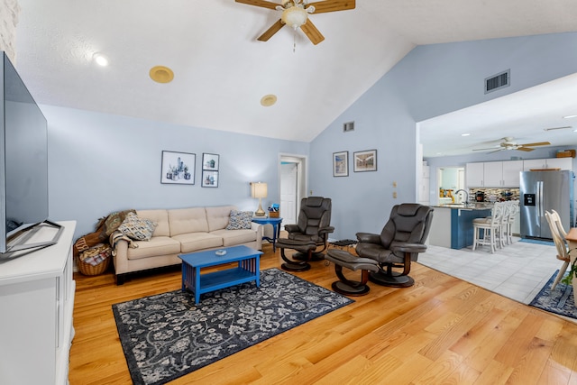 living room with light wood-type flooring, high vaulted ceiling, ceiling fan, and sink