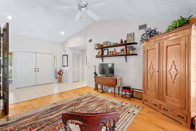 living room featuring a textured ceiling, light hardwood / wood-style floors, ceiling fan, and lofted ceiling