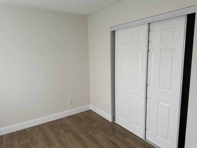 unfurnished bedroom featuring a textured ceiling, dark hardwood / wood-style floors, and a closet