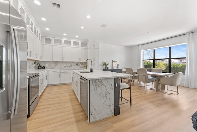 kitchen featuring sink, light hardwood / wood-style floors, a center island with sink, white cabinets, and appliances with stainless steel finishes