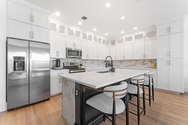 kitchen with sink, an island with sink, a breakfast bar, white cabinets, and appliances with stainless steel finishes