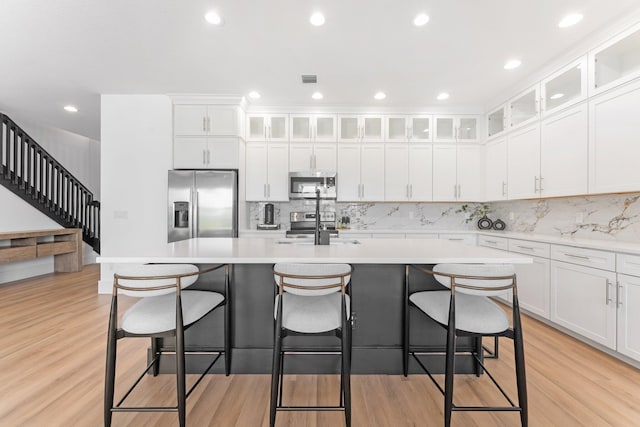 kitchen featuring a center island with sink, white cabinetry, appliances with stainless steel finishes, and light hardwood / wood-style flooring