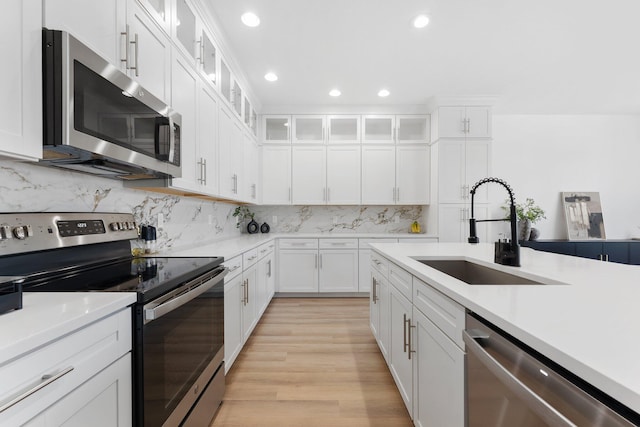 kitchen featuring white cabinetry, sink, stainless steel appliances, tasteful backsplash, and light wood-type flooring