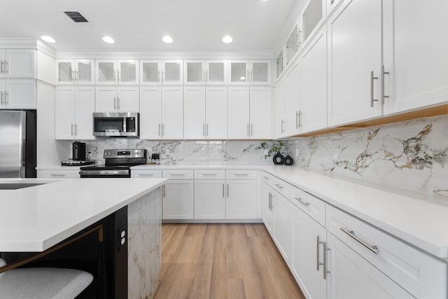 kitchen featuring backsplash, white cabinetry, light hardwood / wood-style floors, and appliances with stainless steel finishes