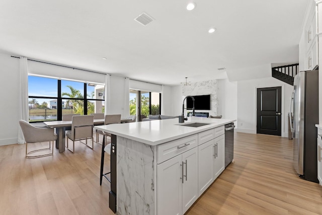 kitchen featuring sink, appliances with stainless steel finishes, a center island with sink, white cabinets, and light wood-type flooring