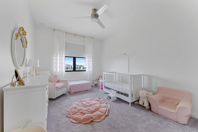 carpeted bedroom featuring a nursery area and ceiling fan