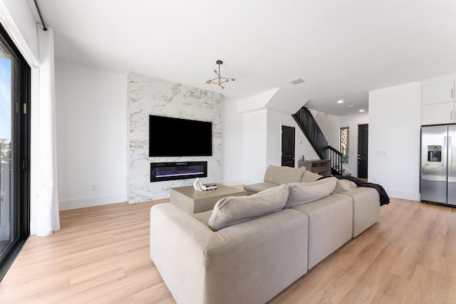 living room featuring a high end fireplace, light wood-type flooring, and an inviting chandelier