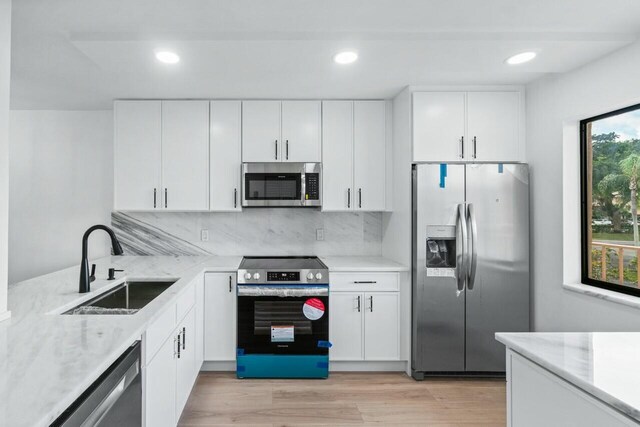 kitchen featuring white cabinetry, decorative backsplash, light hardwood / wood-style floors, and appliances with stainless steel finishes