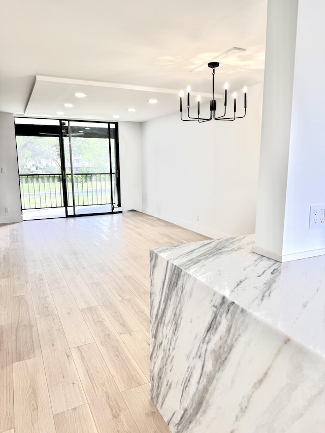 empty room with an inviting chandelier, a wall of windows, and light hardwood / wood-style flooring