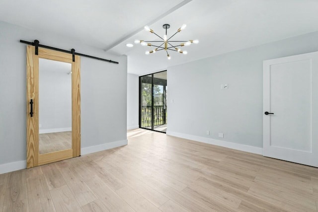 unfurnished room with a notable chandelier, a barn door, expansive windows, and light wood-type flooring