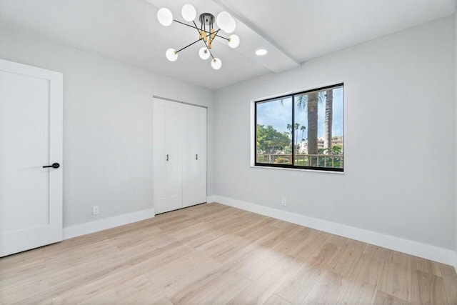 unfurnished bedroom featuring an inviting chandelier, light hardwood / wood-style floors, and a closet