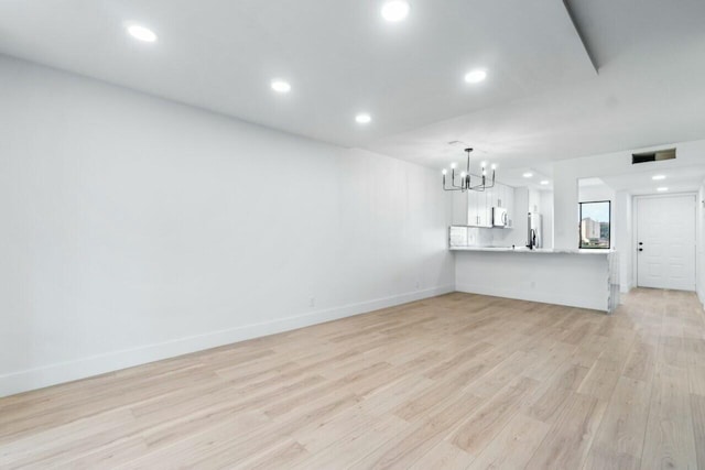 unfurnished living room with an inviting chandelier and light hardwood / wood-style flooring