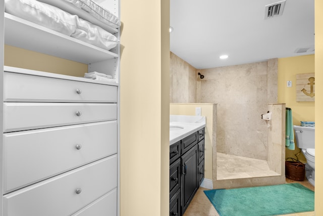 bathroom featuring tile patterned flooring, a tile shower, vanity, and toilet