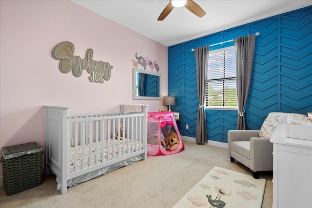 bedroom with light carpet, a nursery area, and ceiling fan