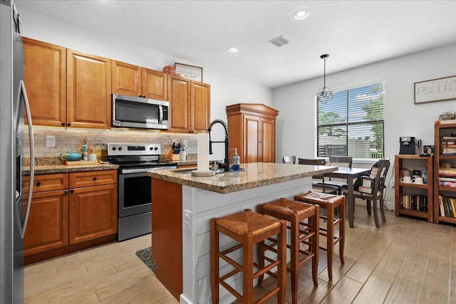 kitchen with stone counters, pendant lighting, a kitchen bar, a center island with sink, and appliances with stainless steel finishes