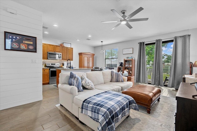 living room with ceiling fan, light hardwood / wood-style flooring, wood walls, and sink