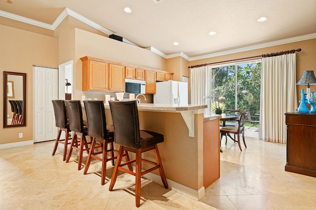 kitchen with white fridge with ice dispenser, crown molding, a textured ceiling, a kitchen bar, and light brown cabinetry