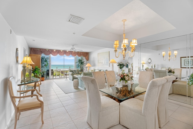 tiled dining space featuring ceiling fan with notable chandelier and a water view