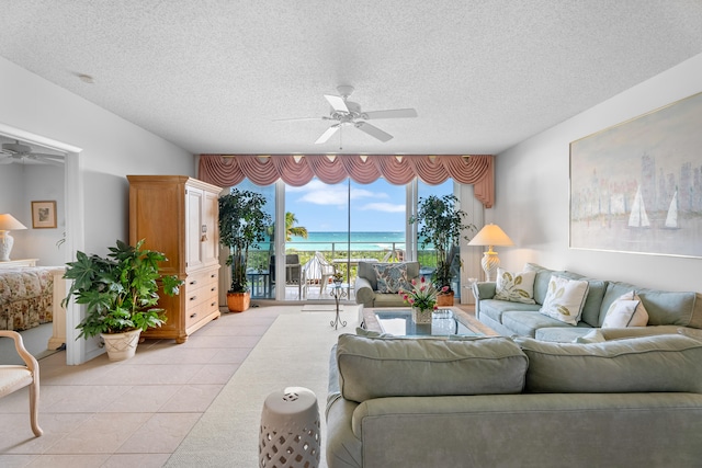 tiled living room featuring ceiling fan, a water view, and a textured ceiling