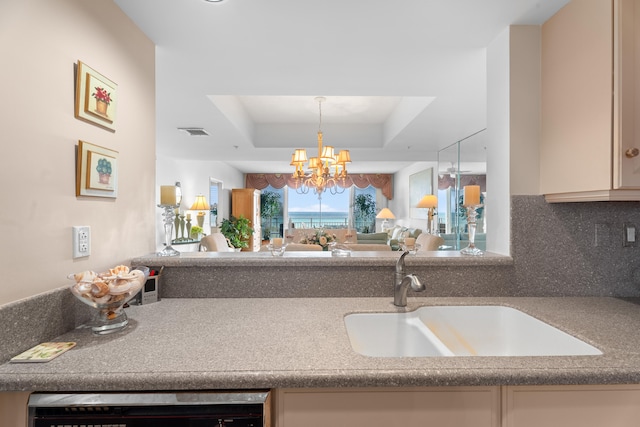 kitchen featuring backsplash, a tray ceiling, sink, dishwasher, and a chandelier