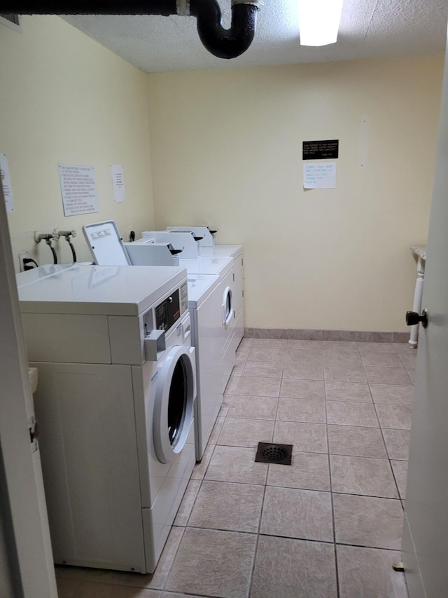 clothes washing area featuring light tile patterned floors, a textured ceiling, and washer and clothes dryer