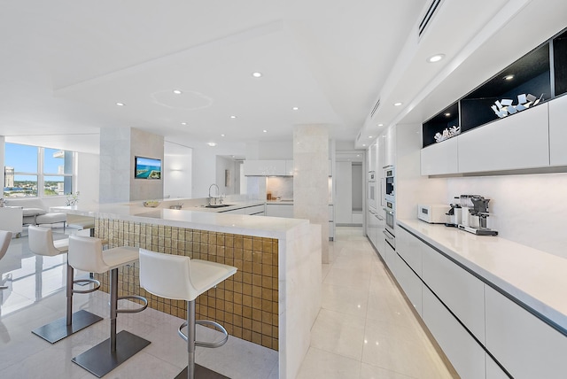 kitchen with white cabinetry, sink, oven, a spacious island, and light tile patterned flooring