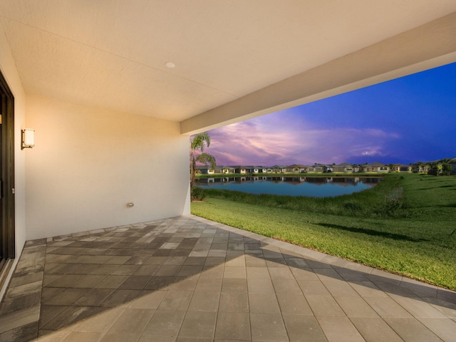 patio terrace at dusk featuring a yard and a water view