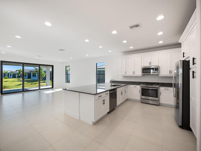 kitchen with dark stone counters, white cabinets, light tile patterned floors, appliances with stainless steel finishes, and kitchen peninsula