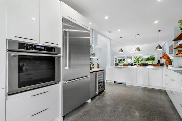 kitchen featuring stainless steel appliances, beverage cooler, white cabinets, decorative light fixtures, and kitchen peninsula