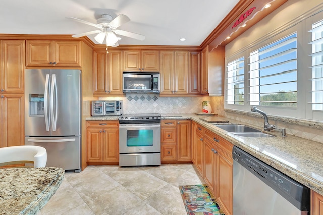 kitchen featuring ceiling fan, sink, stainless steel appliances, light stone counters, and backsplash