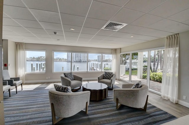 living room with a wealth of natural light, hardwood / wood-style floors, a water view, and a drop ceiling