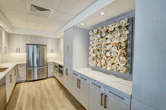 kitchen featuring white cabinets, sink, light hardwood / wood-style flooring, light stone counters, and stainless steel appliances