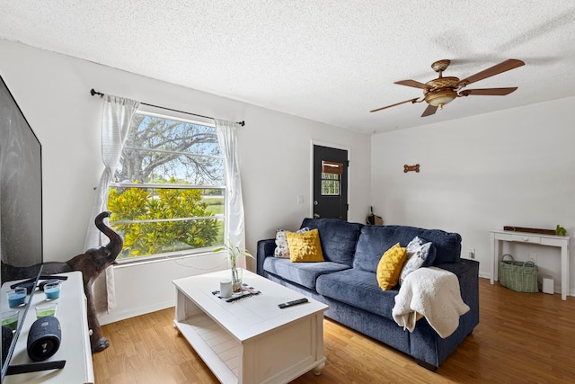 living area featuring light wood-style floors, ceiling fan, and a textured ceiling