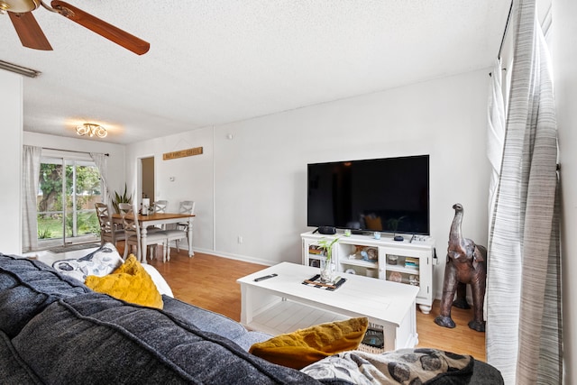 living room featuring light wood-style flooring, baseboards, ceiling fan, and a textured ceiling