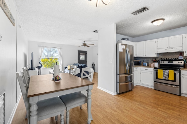 kitchen with light wood finished floors, visible vents, backsplash, appliances with stainless steel finishes, and under cabinet range hood