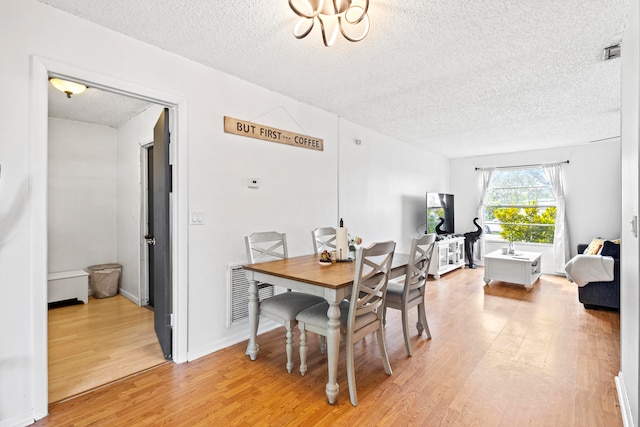 dining space featuring light wood-type flooring, visible vents, and a textured ceiling