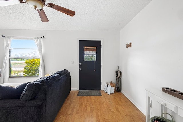 living area featuring light wood-style flooring, baseboards, ceiling fan, and a textured ceiling