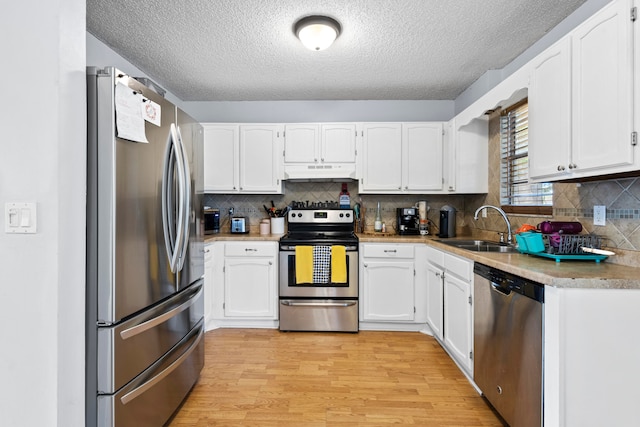 kitchen with light wood-style flooring, under cabinet range hood, stainless steel appliances, a sink, and white cabinetry