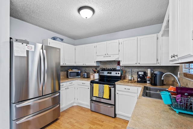 kitchen with light wood finished floors, appliances with stainless steel finishes, white cabinetry, a sink, and under cabinet range hood