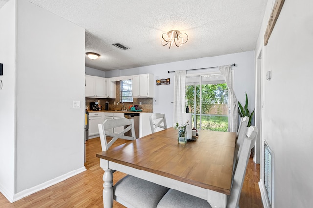 dining room featuring a textured ceiling, light wood-style flooring, visible vents, and baseboards