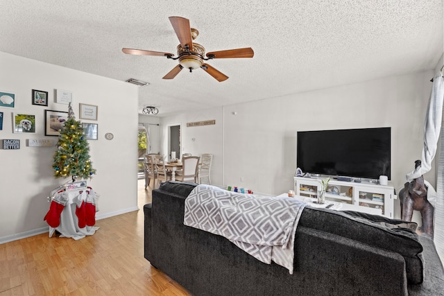 living area featuring baseboards, visible vents, ceiling fan, wood finished floors, and a textured ceiling