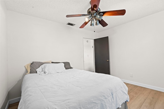 bedroom featuring a textured ceiling, wood finished floors, a ceiling fan, visible vents, and baseboards