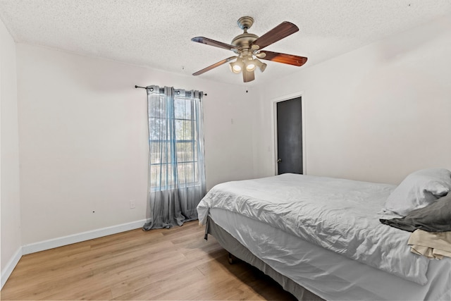 bedroom with ceiling fan, a textured ceiling, baseboards, and wood finished floors